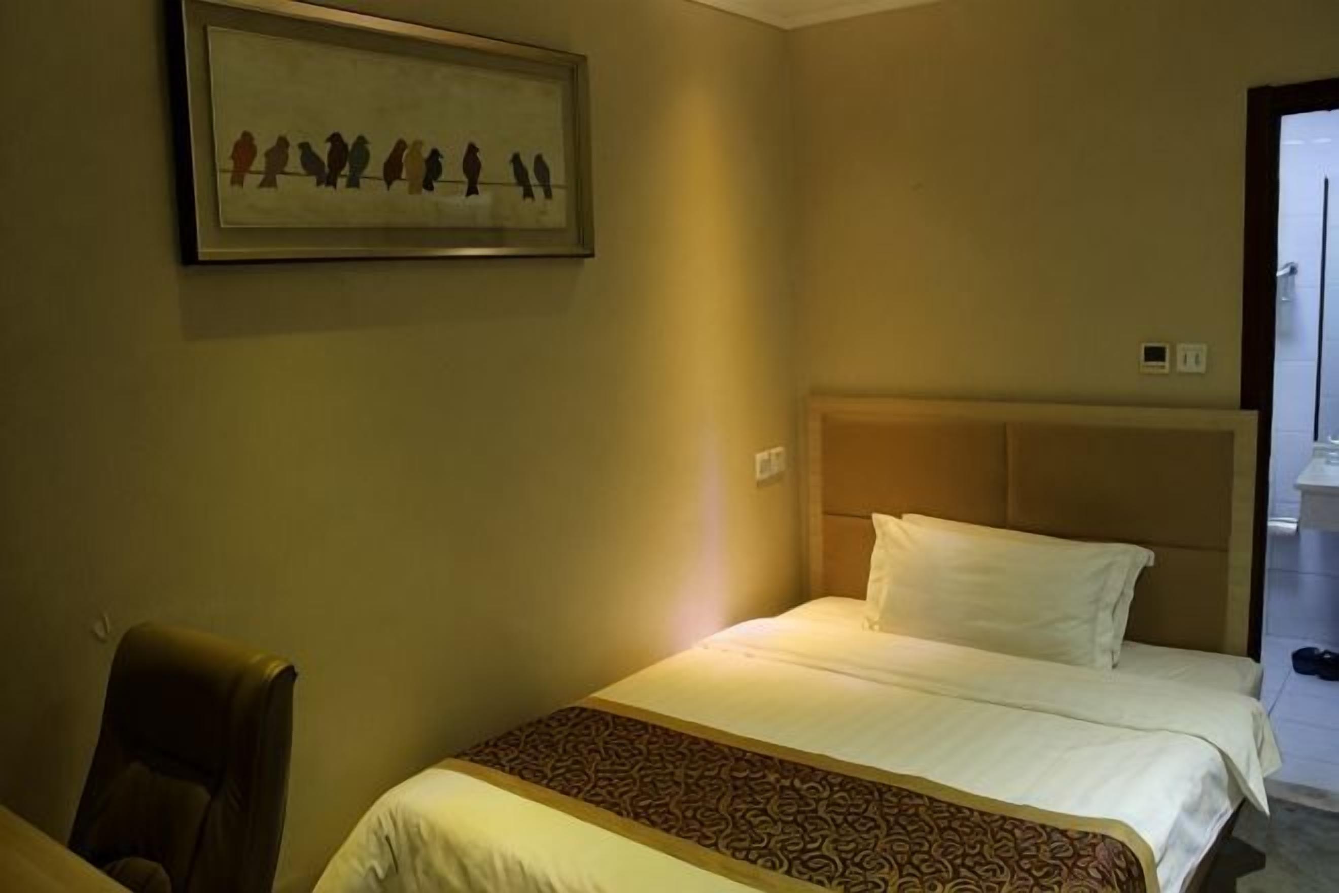Habitación de hotel con cama, una silla, un cuadro en la pared y una puerta que da a un pasillo.
