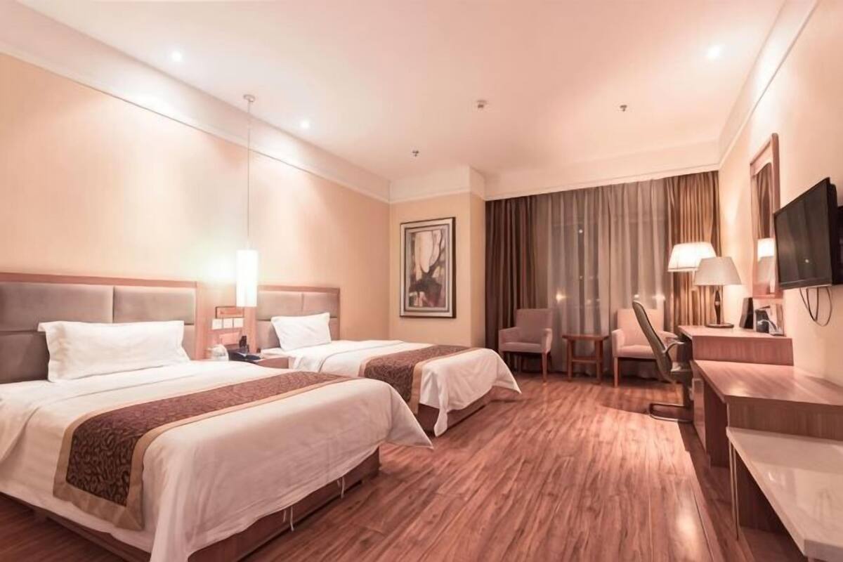 A hotel room with two beds, a desk, a chair, a television, and a large window with curtains.
