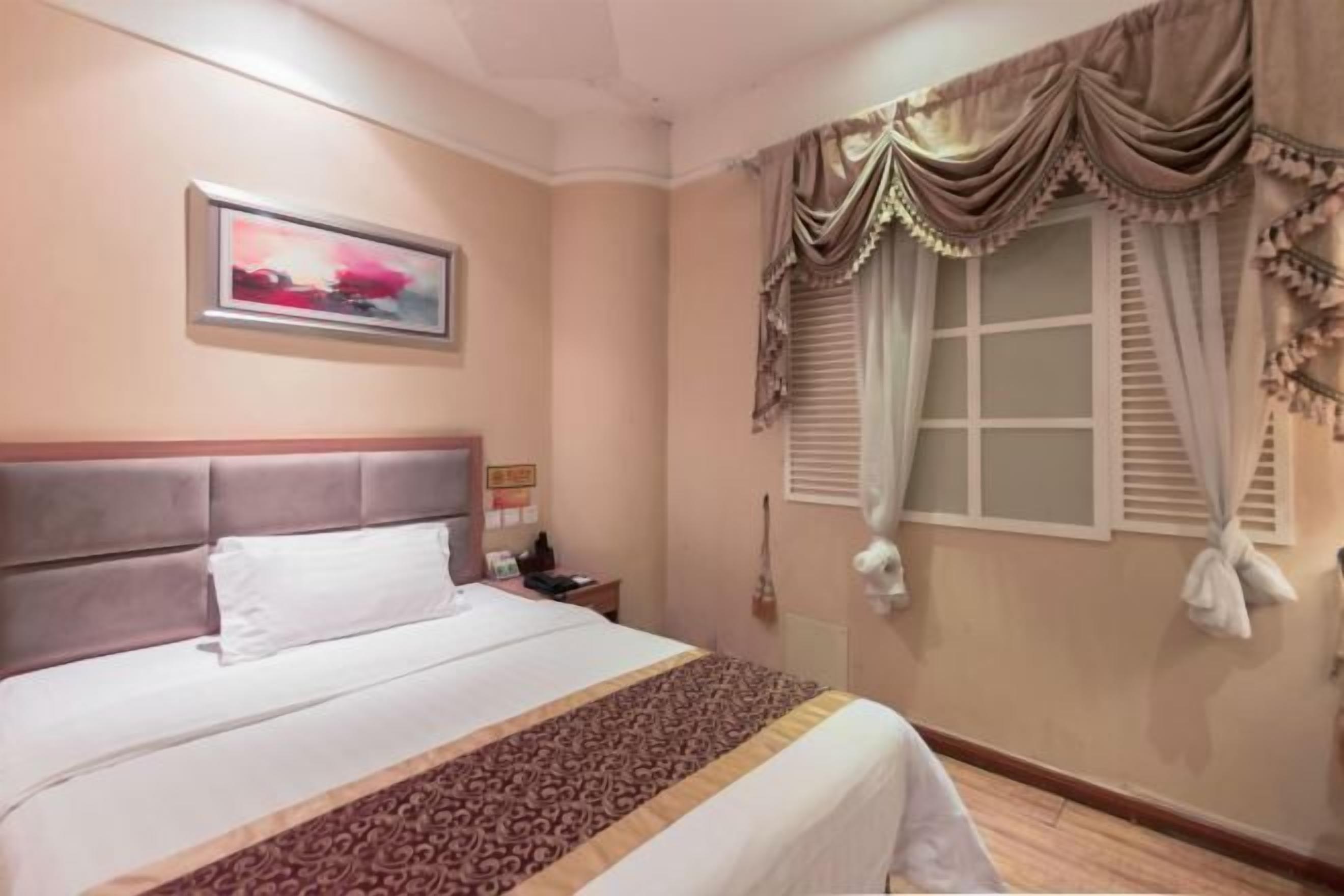 A hotel room with a bed, a nightstand, a telephone, a window with curtains, and a painting on the wall.