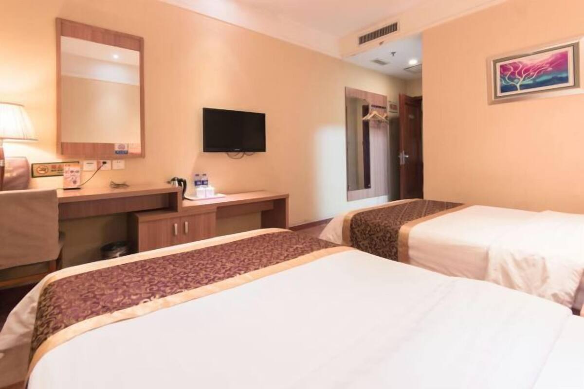A hotel room with two beds, a desk with a chair, a television, and a mirror.