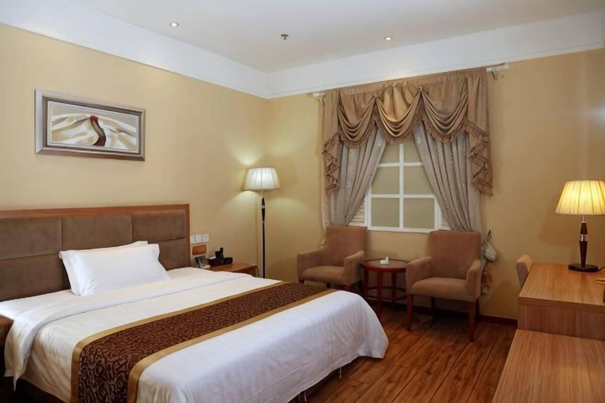A hotel room with a large bed, two armchairs, a small table, a lamp, and a window with curtains.