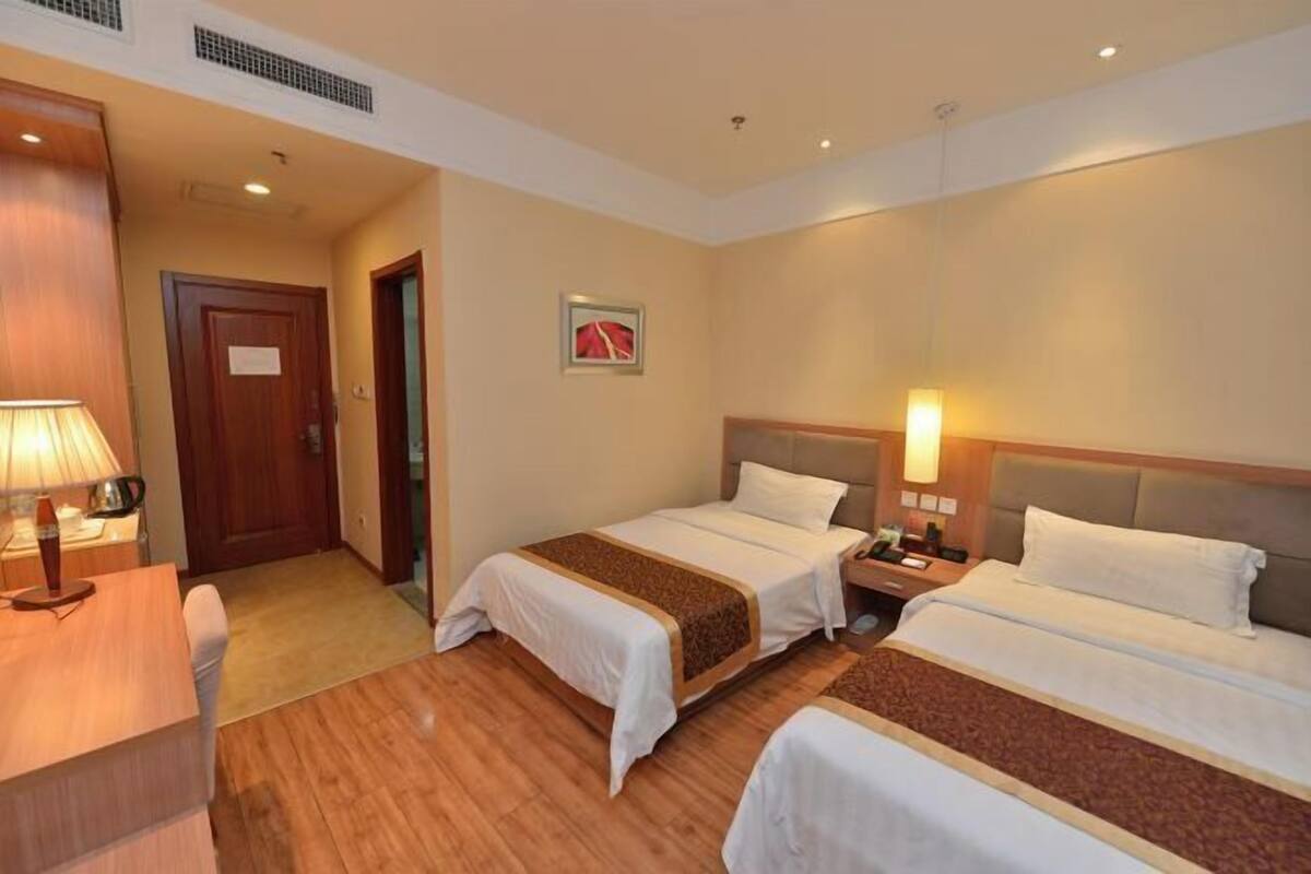 A hotel room with two beds, a desk, a lamp, and a door.