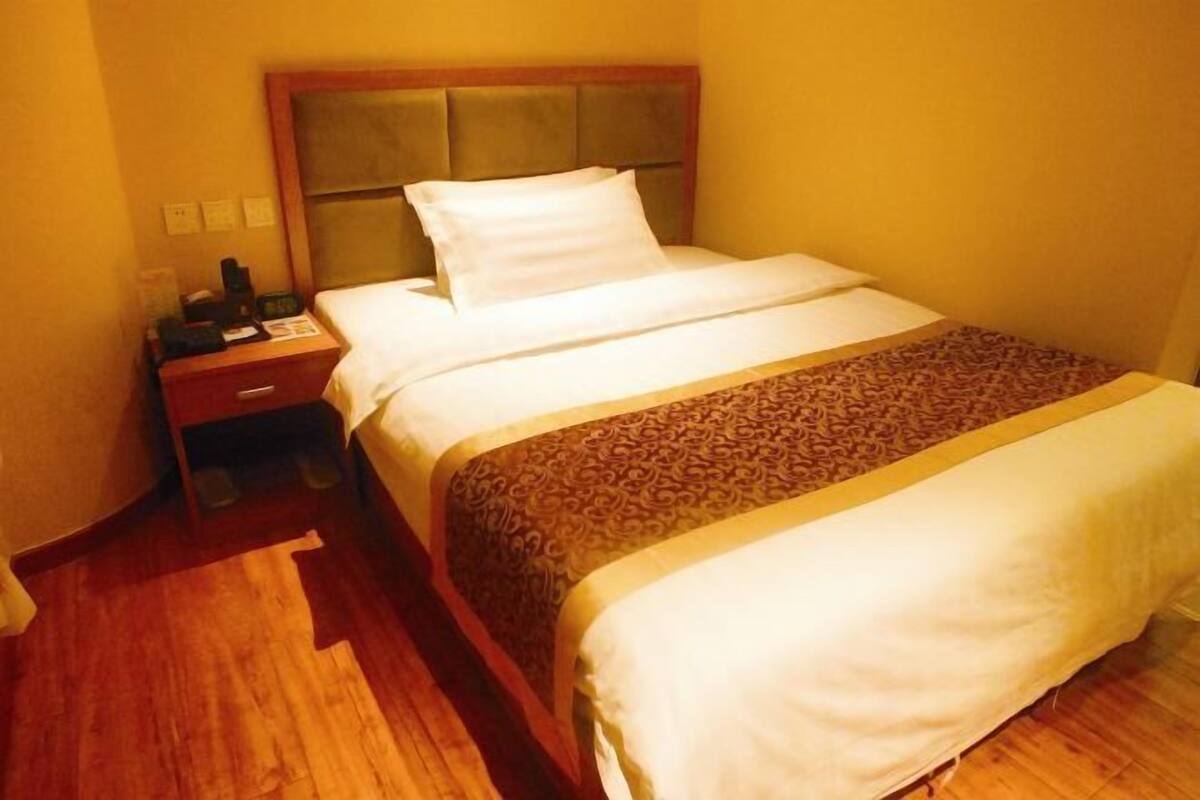 A hotel room with a bed, a nightstand, a drawer, and a patterned rug.