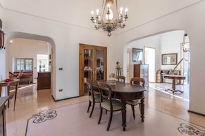 A dining area with a round table, chairs, and a chandelier. There is a wooden cabinet and a door leading to another room.