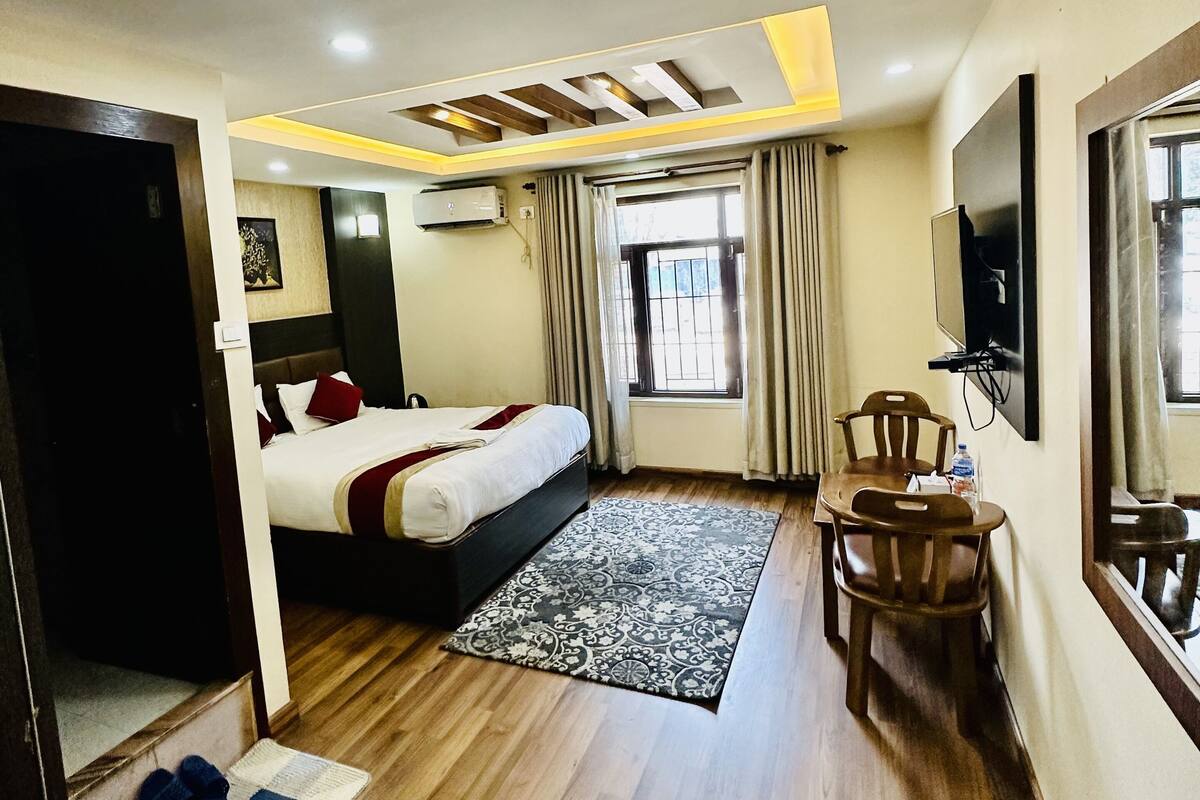 A hotel room with a bed, a desk, a chair, a TV, and a window with curtains.