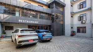 A modern building with a restaurant sign, two cars parked in front, and a paved courtyard. - Hotel Airport Deepshree (Kathmandu)
