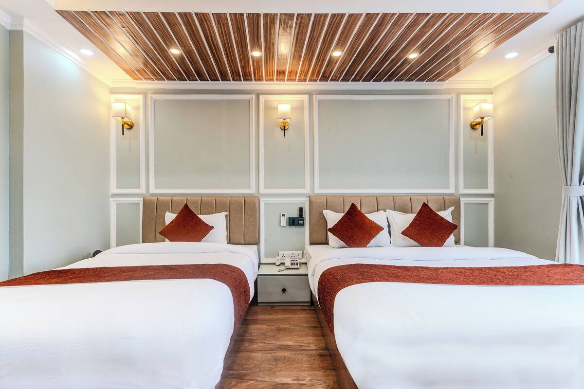 A hotel room with two beds, wooden ceiling, wall-mounted lights, and a nightstand with a phone and charger.