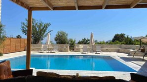 A swimming pool with lounge chairs and umbrellas, surrounded by a wooden pergola and stone walls. - Peacefull Stone-Built Villa (Mylopotamos)
