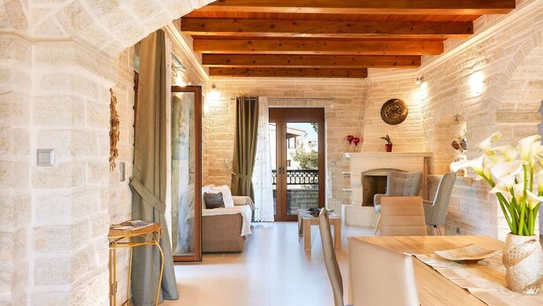 A cozy room with a stone wall, wooden ceiling beams, a fireplace, and a dining area with a table and chairs. - Peacefull Stone-Built Villa (Mylopotamos)