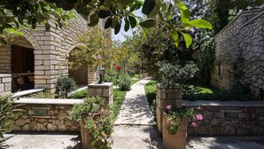 A stone building with a narrow pathway leading to a door, surrounded by lush greenery and potted plants. - Peacefull Stone-Built Villa (Mylopotamos)