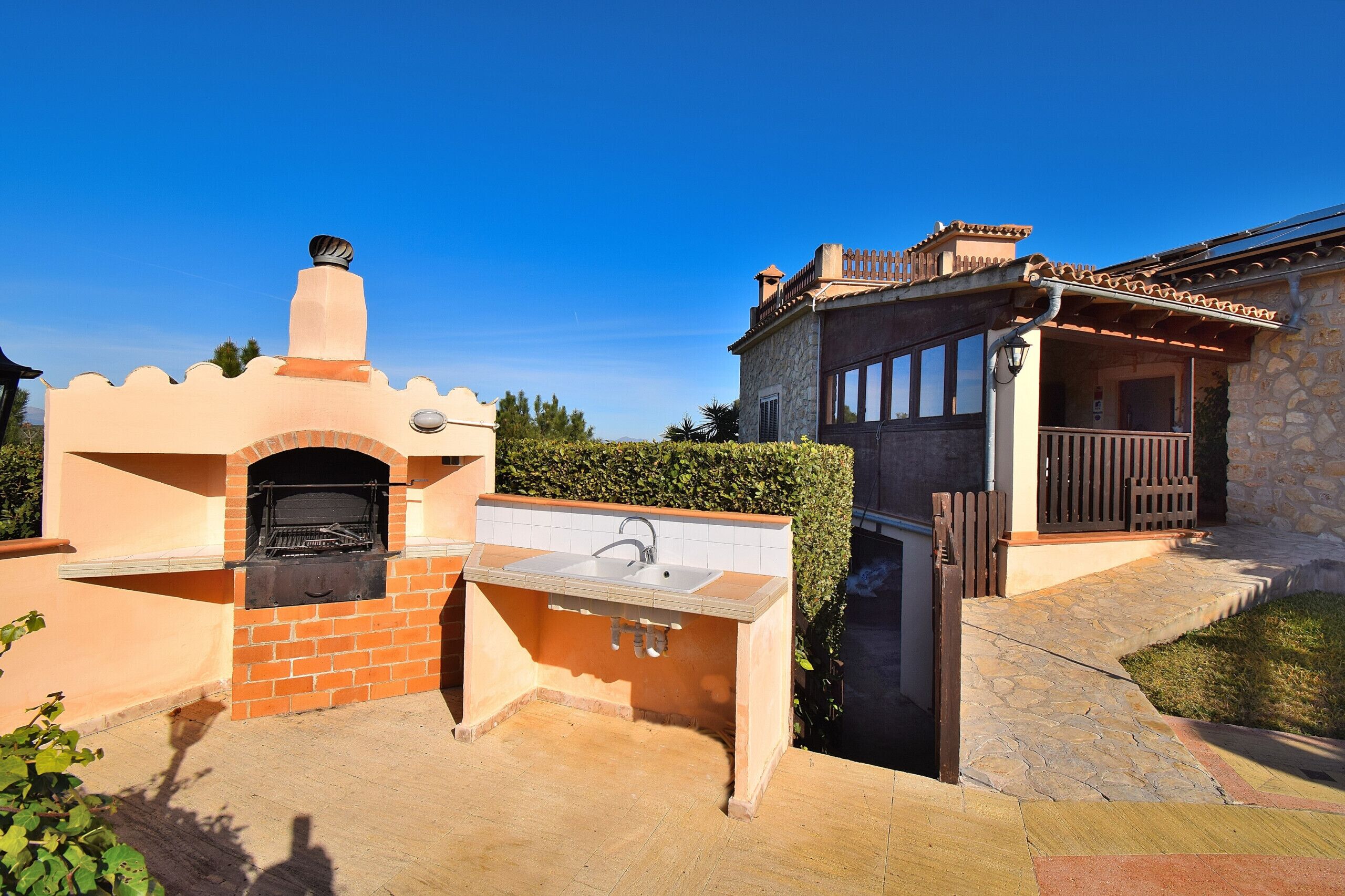 An outdoor kitchen with a brick oven and sink, adjacent to a stone building with a balcony.