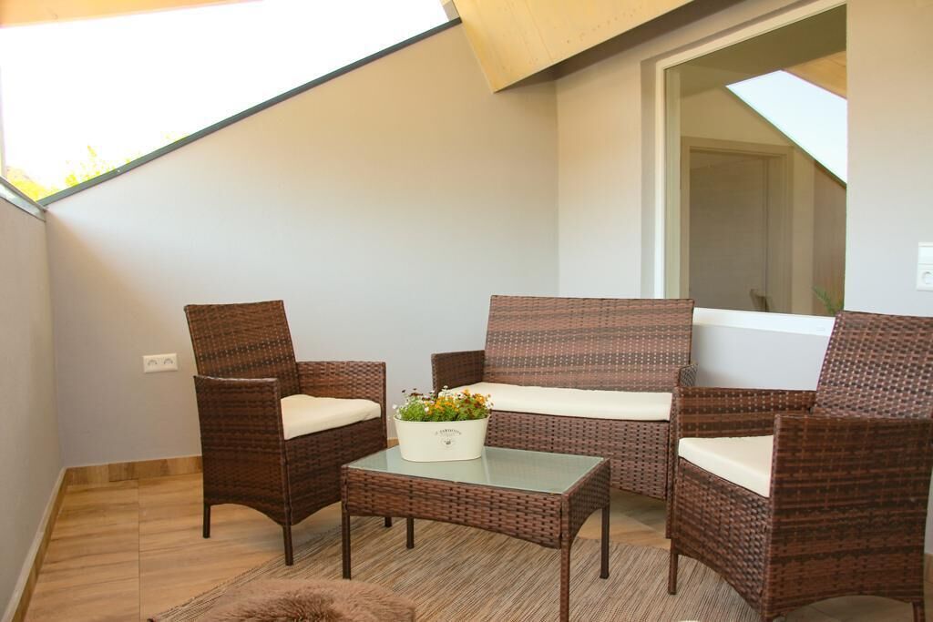 A balcony with wicker furniture, a glass table, and a potted plant.