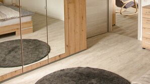 Ein Schlafzimmer mit großem Spiegel, Holzschrank und einem Bett mit grauem Teppich.