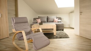 Ein Schlafzimmer im Loft-Stil mit schrägen Wänden, einem grauen Sofa, einem Holztisch und einem Schaukelstuhl.