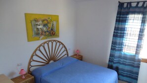 A bedroom with a bed, a nightstand, a lamp, a painting on the wall, and a window with curtains. - Three-room apartment 7 seats second floor with sea view veranda (Rena Majore)