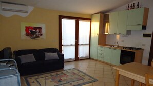 A compact living space with a sofa, a dining table, a kitchen area with cabinets, and a sliding glass door leading to an outdoor area. - Three-room apartment 7 seats second floor with sea view veranda (Rena Majore)