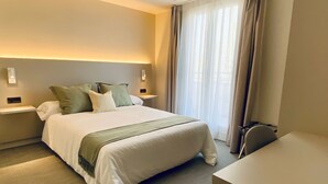 Een moderne hotelkamer met een netjes opgemaakt bed, een nachtkastje, een bureau en een groot raam met gordijnen.
