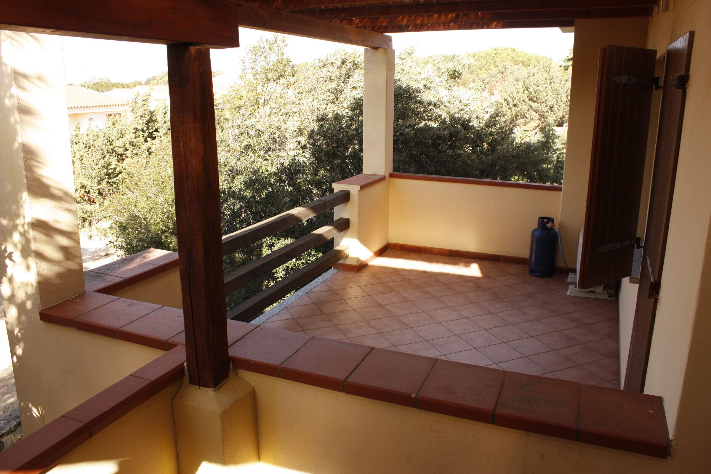 A balcony with a tiled floor, wooden railings, and a view of trees and buildings.