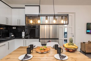 A modern kitchen with white cabinets, a stainless steel refrigerator, a wooden dining table with plates, cups, and a fruit bowl. - Luxury Villa Solis (Karlobag)