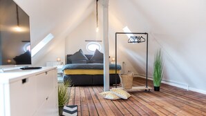 A cozy attic bedroom with a sloped ceiling, a bed with pillows, a hanging light fixture, and a potted plant. - fewo1846 - flensBURG / centrally located, elegant maisonette apartment on the 4t (Flensburg)