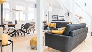 A modern living room with a black sofa, wooden flooring, and a dining area with a table and chairs. - fewo1846 - flensBURG / centrally located, elegant maisonette apartment on the 4t (Flensburg)