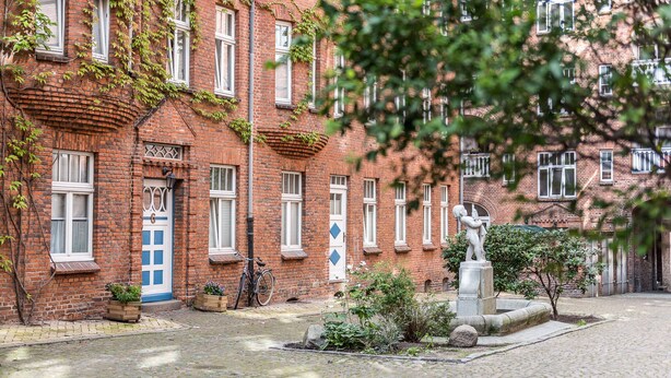 A red brick building with white windows and a blue door. There is a statue in front of the building and a bicycle parked against the wall. - fewo1846 - flensBURG / centrally located, elegant maisonette apartment on the 4t (Flensburg)