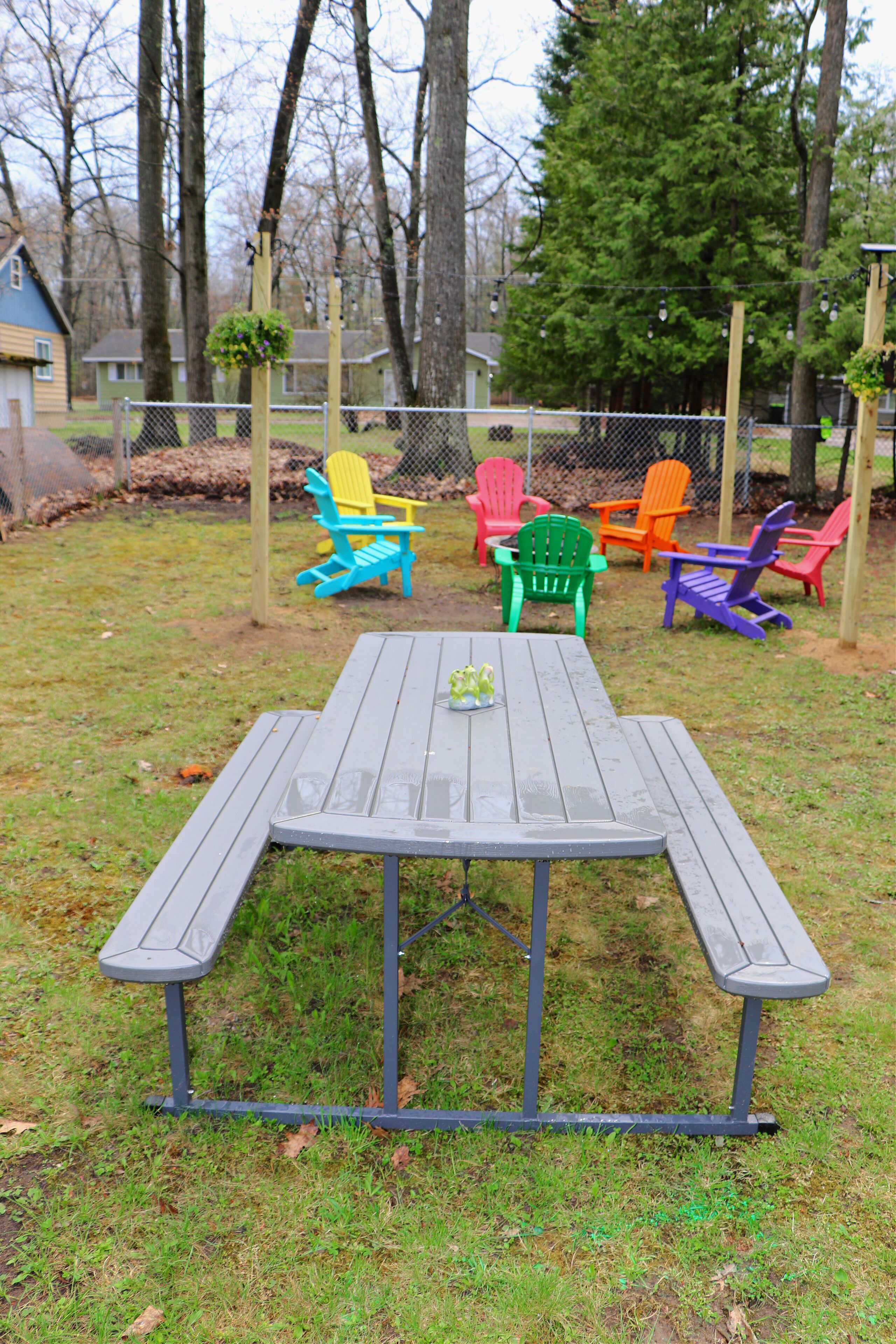A picnic table with a metal frame and benches, surrounded by colorful Adirondack chairs.