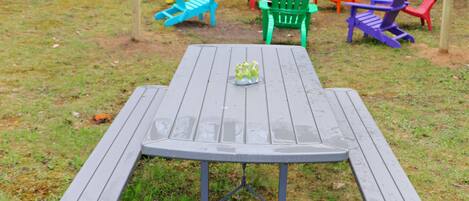 A picnic table with a metal frame and benches, surrounded by colorful Adirondack chairs.