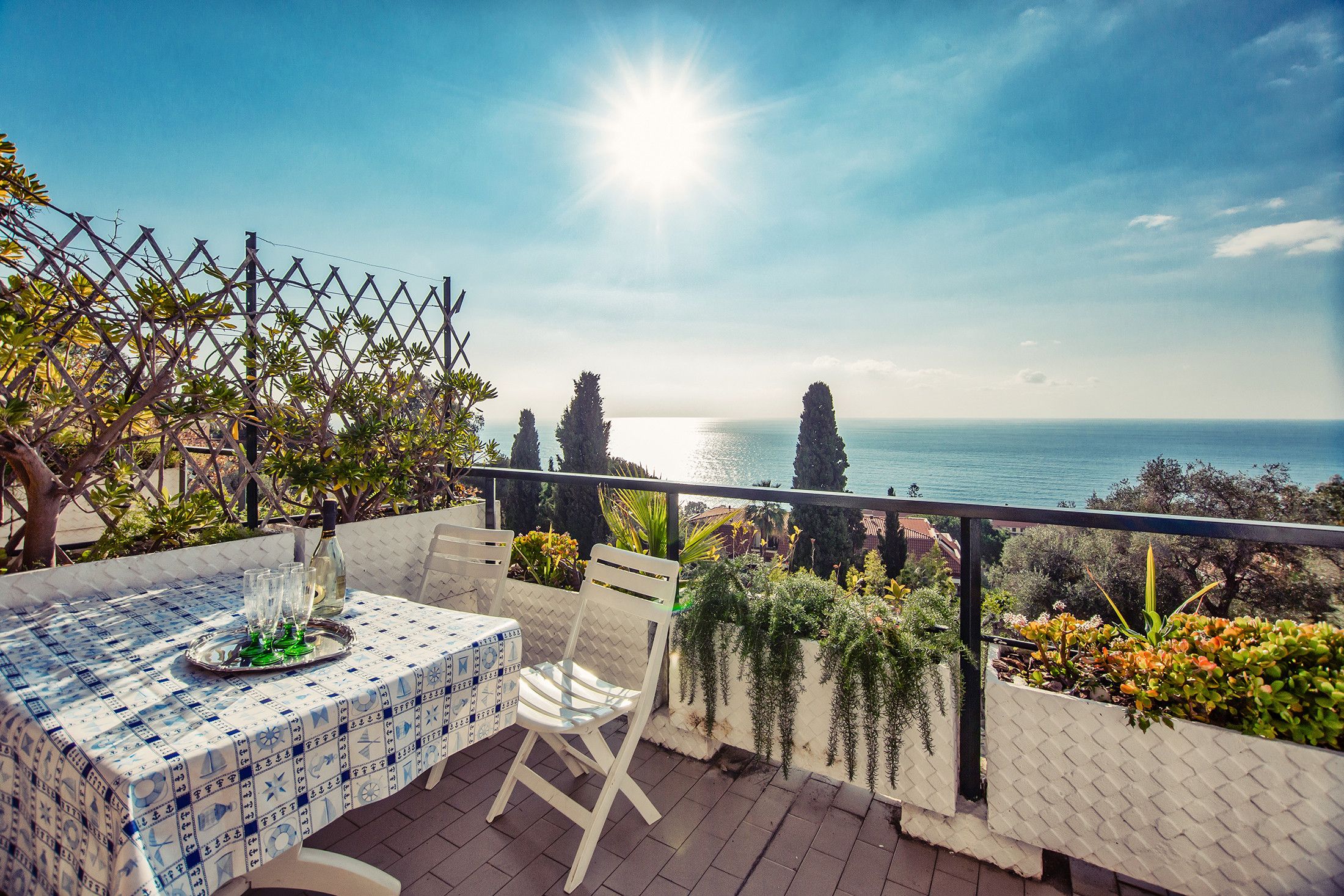 A terrace with a table set for dining, overlooking a coastal view.