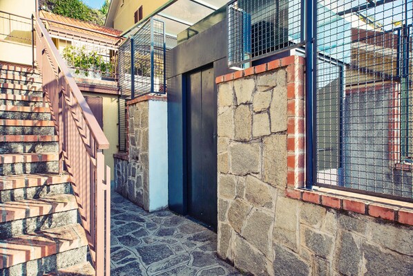 A narrow stone-walled corridor with a metal railing, a door, and a window with a metal grid.