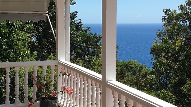Un balcon abrité avec un sol à carreaux, des balustrades blanches, une lanterne suspendue et un pot de fleurs contenant des fleurs roses.