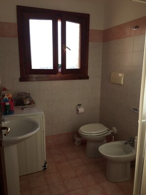 Ein kleines Badezimmer mit Fenster, Waschbecken, Toilette und Bidet.