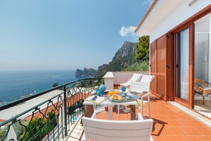 Ein Balkon mit Frühstückstisch, der Blick auf die Küste mit Bergen und dem Meer freigibt.