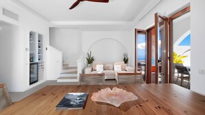 Ein modernes Wohnzimmer mit einem Holzesstisch, einer Sofagarnitur, einer Treppe und Blick ins Freie.
