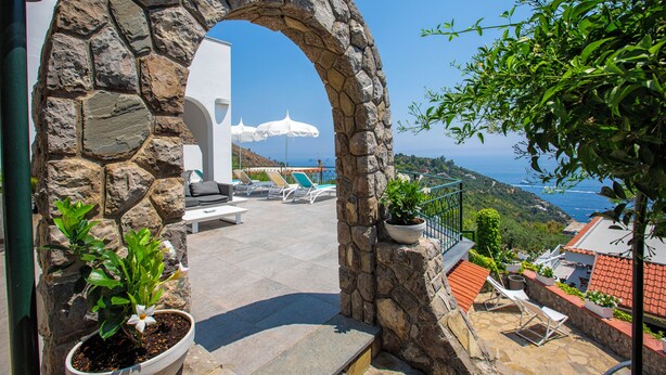 Ein steinerer Bogen führt zu einer Terrasse mit Sitzgelegenheiten und Meerblick.