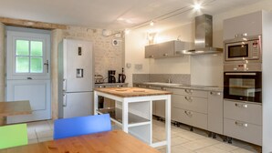 A compact kitchen with a refrigerator, microwave, oven, and a wooden table with chairs. - MOULIN DE PREZIER - Gîte Nénuphar (Cherves-Richemont)