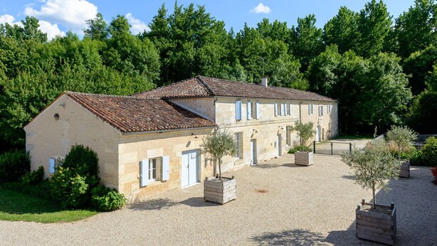 A two-story stone building with a tiled roof, surrounded by a gravel courtyard and small trees. - MOULIN DE PREZIER - Gîte Nénuphar (Cherves-Richemont)