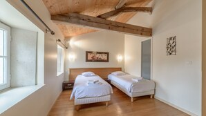A bedroom with two single beds, wooden flooring, a wooden ceiling, and a large window. - MOULIN DE PREZIER - Gîte Nénuphar (Cherves-Richemont)