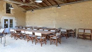 A rustic dining area with wooden tables and chairs, a high wooden ceiling, and a stone wall. - MOULIN DE PREZIER - Gîte Nénuphar (Cherves-Richemont)