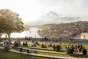 A riverside park with people sitting on steps, overlooking a cityscape with buildings and a river. - Casa Azul - Jardim do Morro (Vila Nova de Gaia)