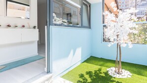 Ein modernes Interieur mit einem weißen Waschtisch, einem großen Fenster und einem kleinen Kunstbaum auf einer Fläche aus Kunstrasen.
