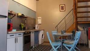 A compact kitchen with a washing machine, a microwave, and a coffee maker. There is a table with chairs and a staircase leading to an upper level. - Character property (CHARBONNIERES LES VIEILLES)