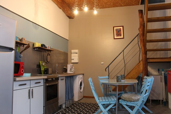 Cocina compacta equipada con microondas, horno y lavadora. Hay un comedor con mesa y sillas.