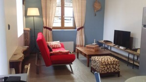 A compact living room with a red armchair, a wooden table, a patterned ottoman, a television, and a window with curtains. - Character property (CHARBONNIERES LES VIEILLES)
