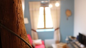 A close-up of a wooden surface with a metal rod, a red sofa, and a window with curtains in the background. - Character property (CHARBONNIERES LES VIEILLES)