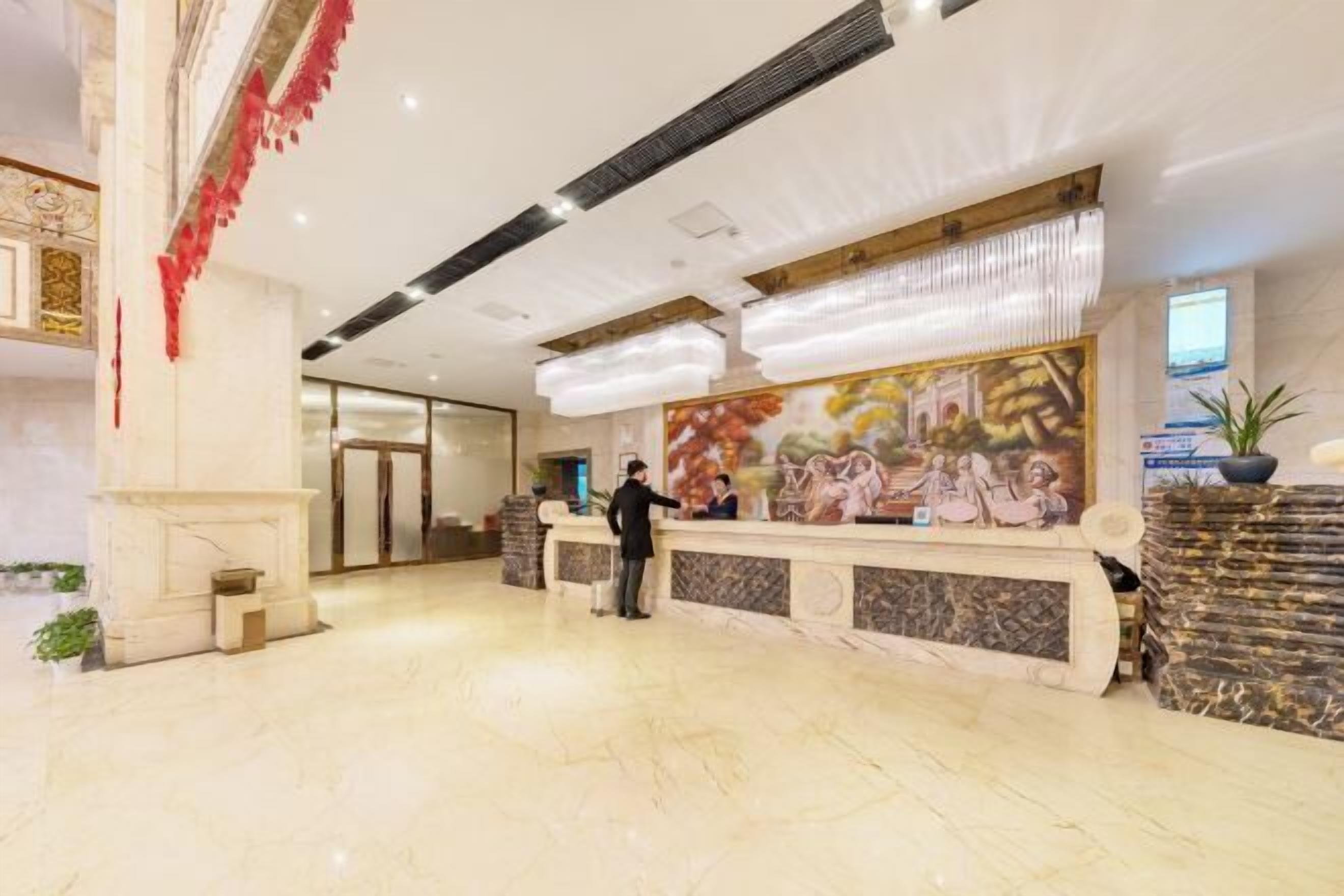 A hotel lobby with a marble reception desk, a fireplace, and a mural on the wall.