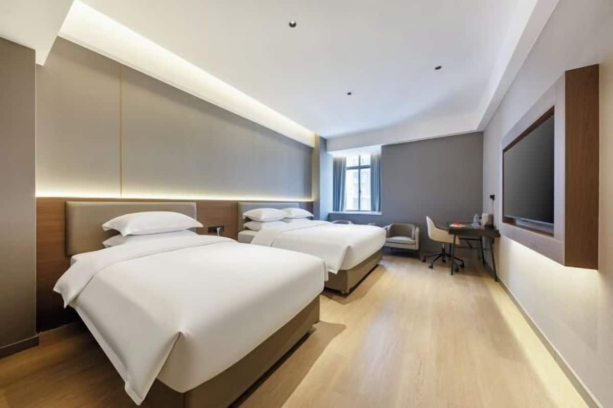 Une chambre d’hôtel avec trois lits, un bureau, une chaise et un grand écran de télévision.
