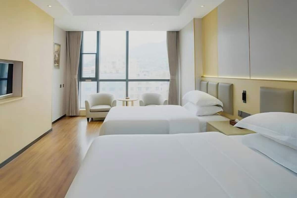 Une chambre d’hôtel avec deux lits, une télévision, une petite table et une vue sur la ville grâce à de grandes fenêtres.