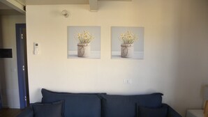 A living room with a dark blue sofa, two wall-mounted paintings of flowers, and a white radiator. - Only 20 min from Olbia: charming 2-bedroom apartment in San Pantaleo with wifi (San Pantaleo)