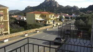 A balcony with a metal railing overlooking a street with buildings and a mountain in the background. - Only 20 min from Olbia: charming 2-bedroom apartment in San Pantaleo with wifi (San Pantaleo)